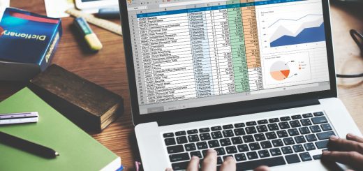 Open laptop showing a detailed spreadsheet with tables and two charts on a desk, surrounded by notebooks and office supplies.