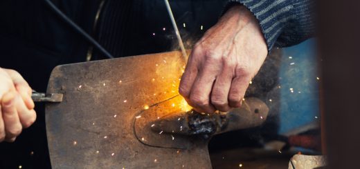 Close-up of hands using a grinding tool on a metal plate, sparks flying around the work area.