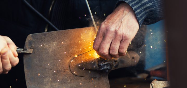 Close-up of hands using a grinding tool on a metal plate, sparks flying around the work area.