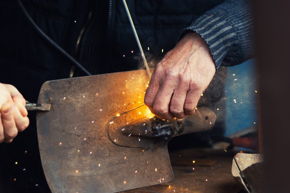 Close-up of hands using a grinding tool on a metal plate, sparks flying around the work area.