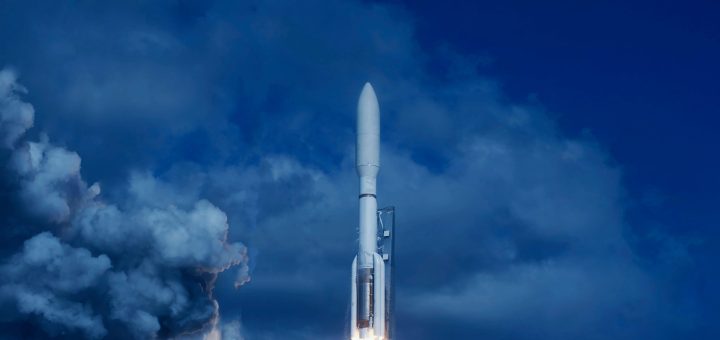 Rocket lifting off from a launch pad, blue sky and dramatic white exhaust plumes behind it