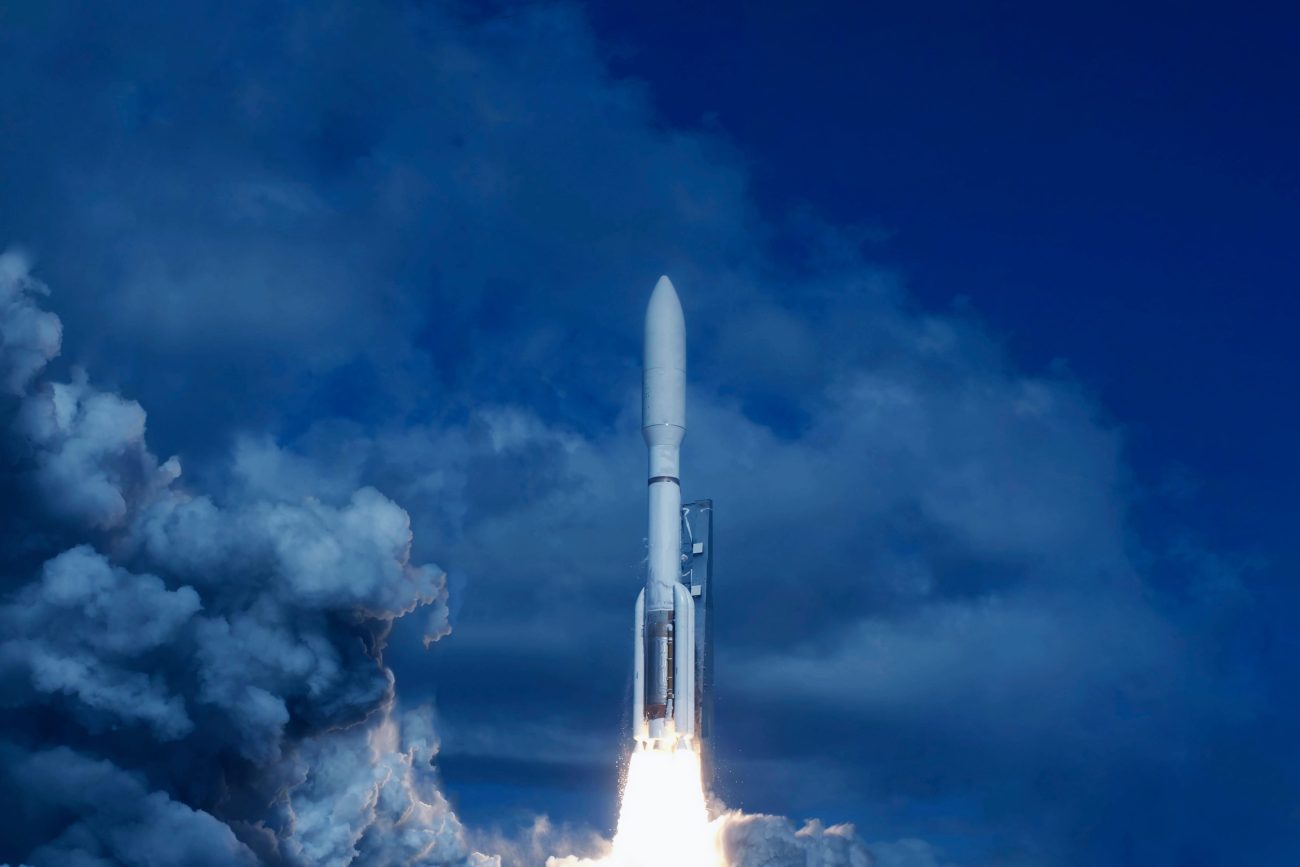 Rocket lifting off from a launch pad, blue sky and dramatic white exhaust plumes behind it