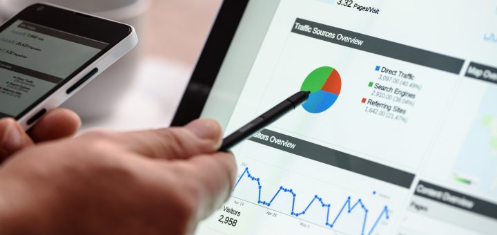 Person uses a stylus on a tablet to view analytics dashboard with a colorful pie chart and line graph showing visitors and traffic sources