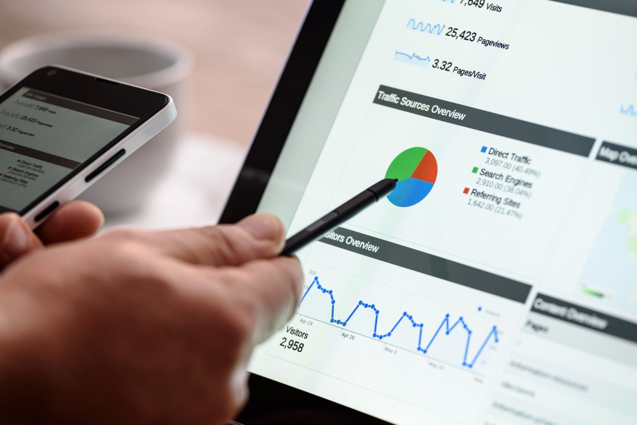 Person uses a stylus on a tablet to view analytics dashboard with a colorful pie chart and line graph showing visitors and traffic sources