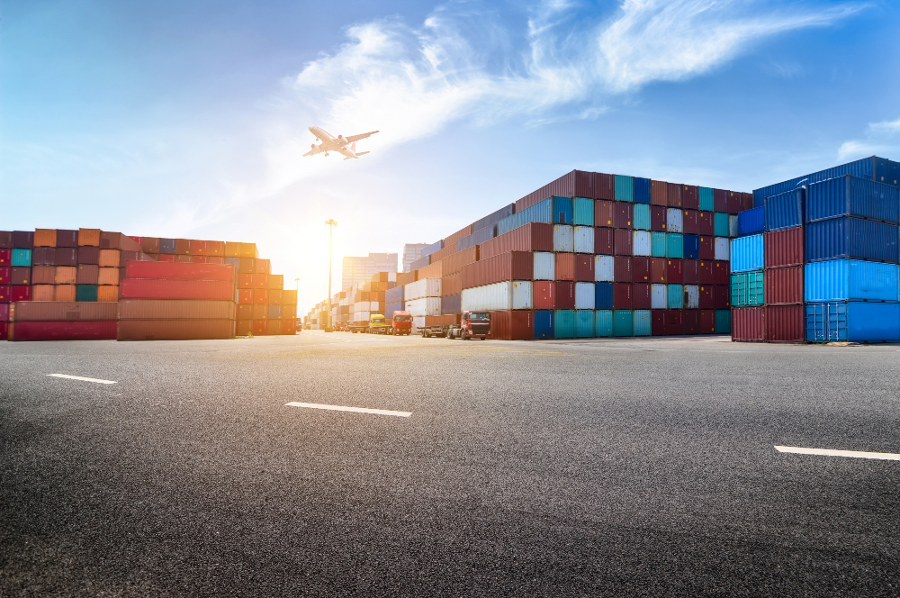 772686 - VSI Consulting | Negocios10.Com Shipping yard with stacked colorful cargo containers and a plane taking off in a bright blue sky