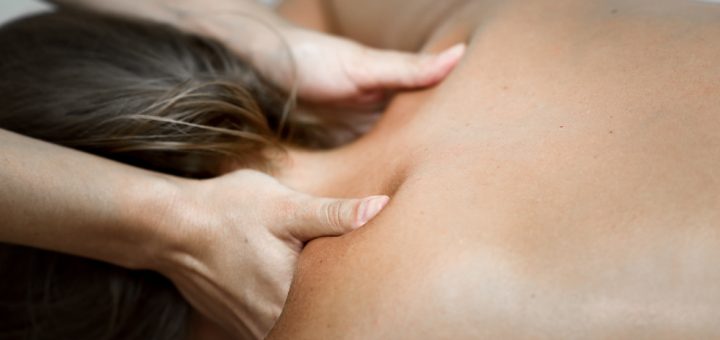 Therapist's hands massage a person's upper back and neck during a therapy session.