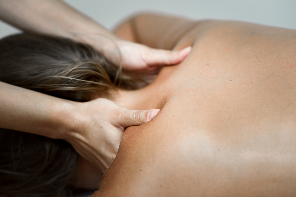 Therapist's hands massage a person's upper back and neck during a therapy session.