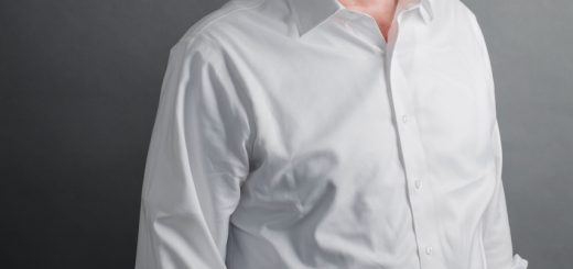 Professional head-and-shoulders portrait of a middle-aged man in a white shirt and dark trousers, looking at the camera against a gray backdrop.