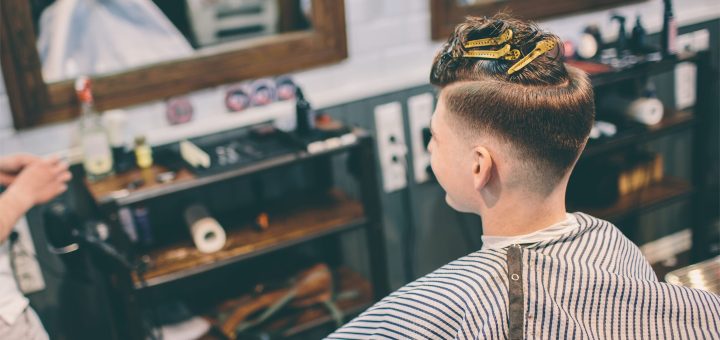 Customer sits in a barber chair with a freshly trimmed undercut, mirrors and barber station in the background.