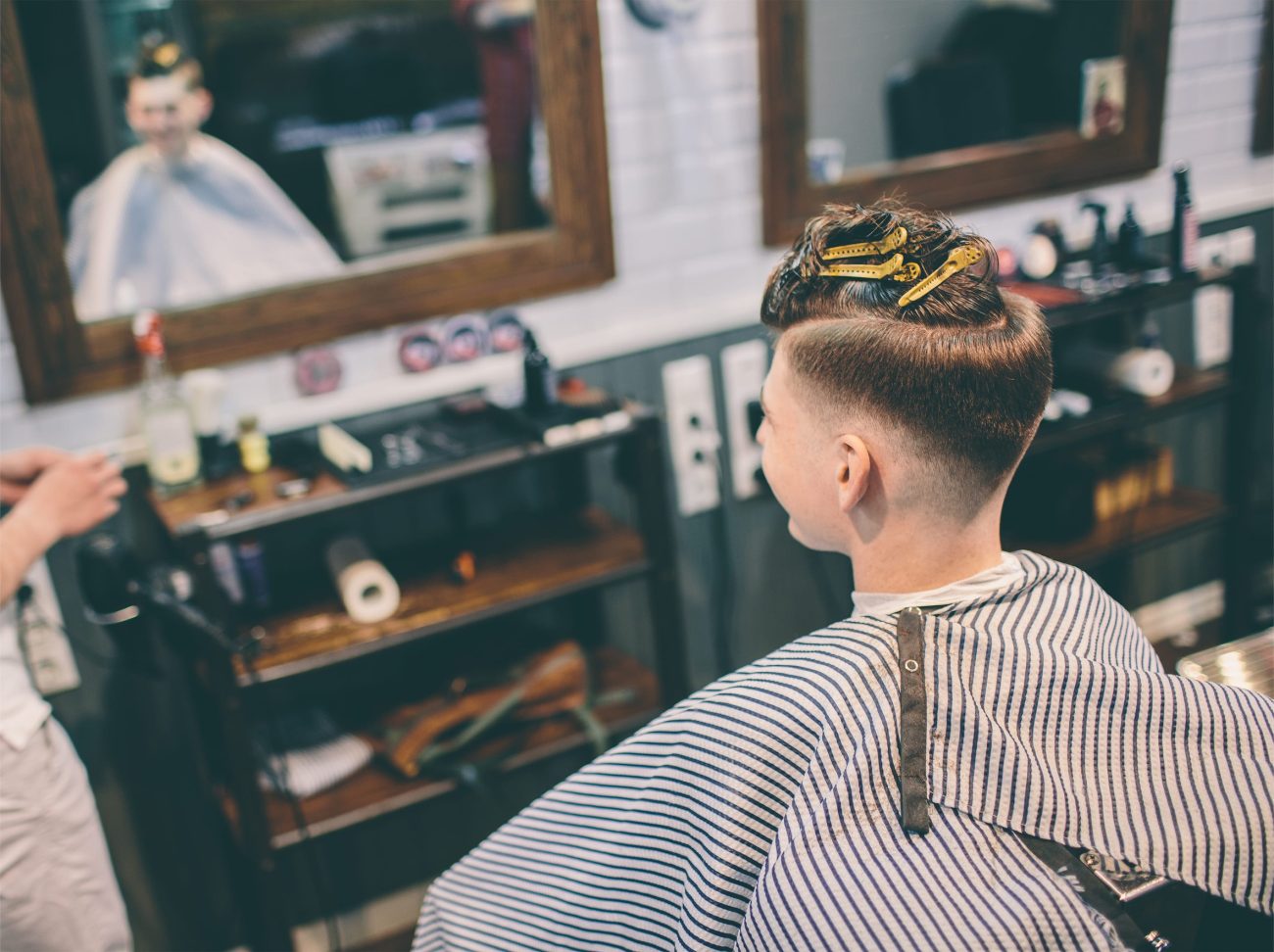 hairstylist and plesed man client with haircut looking in mirror | Negocios10.Com Customer sits in a barber chair with a freshly trimmed undercut, mirrors and barber station in the background.
