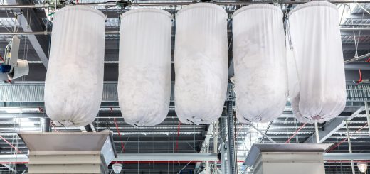 Four large white fabric filter bags suspended from a metal framework in an industrial dust-collection system.