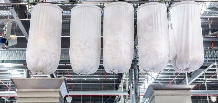 Four large white fabric filter bags suspended from a metal framework in an industrial dust-collection system.