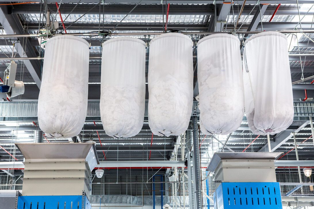 Four large white fabric filter bags suspended from a metal framework in an industrial dust-collection system.