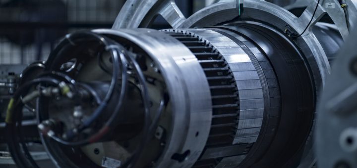 Large industrial turbine component with circular metal sections and attached cables in a workshop.