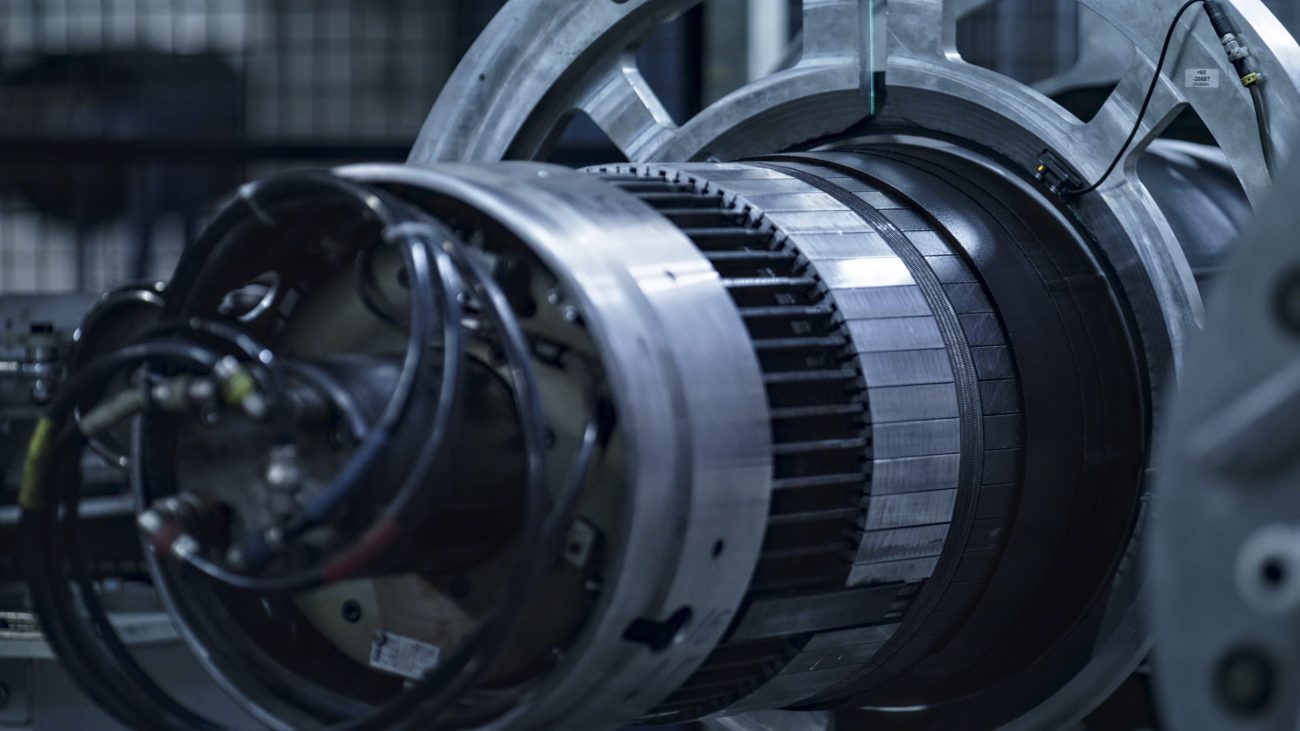 778556 Volta | Negocios10.Com Large industrial turbine component with circular metal sections and attached cables in a workshop.