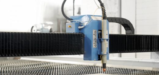Blue CNC laser cutter head moves along a gantry over a sheet of metal being cut in a factory setting.