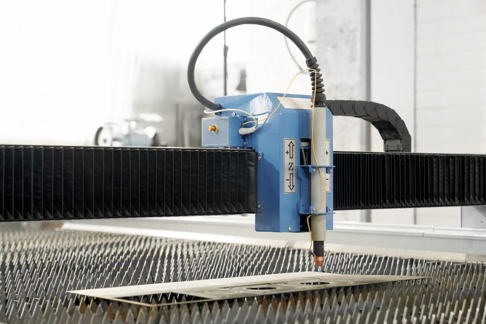 Blue CNC laser cutter head moves along a gantry over a sheet of metal being cut in a factory setting.