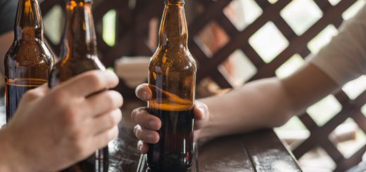 Hands holding beer bottles around a wooden table at an outdoor gathering.