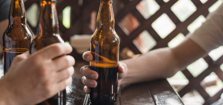 Hands holding beer bottles around a wooden table at an outdoor gathering.
