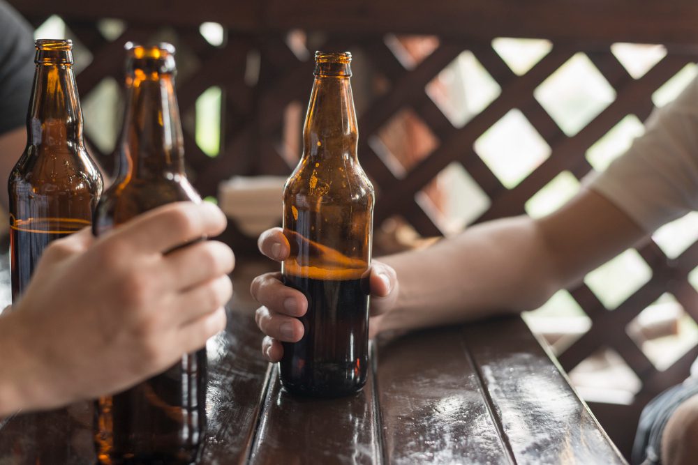 Hands holding beer bottles around a wooden table at an outdoor gathering.