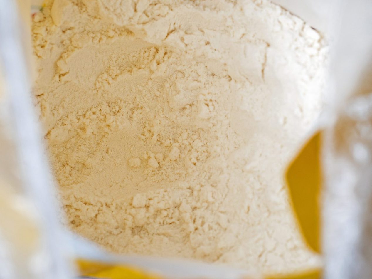 Close-up top view of a bag of white wholemeal flour | Negocios10.Com Close-up of pale flour powder inside a clear bag with yellow packaging accents.